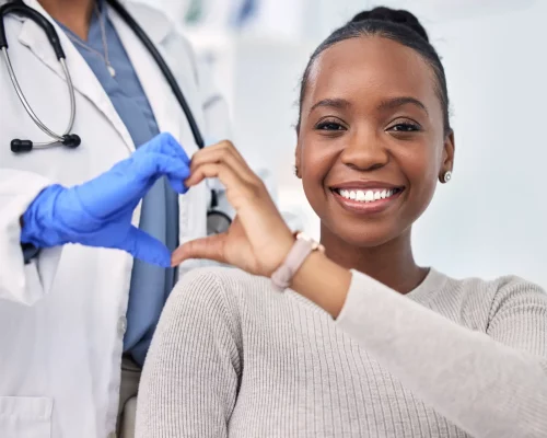 Black woman, patient and doctor with smile, consultation and heart emoji for cardio health, checkup and appointment. Happiness, support and wellness for medicine, healthcare and physical examination